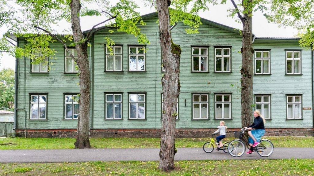 two cycling people passing gray wooden house