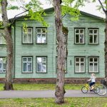 two cycling people passing gray wooden house