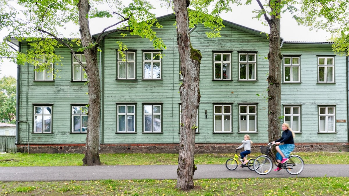 two cycling people passing gray wooden house