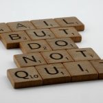 Wooden Scrabble tiles arranged to spell 'Fail but do not quit,' inspiring determination.