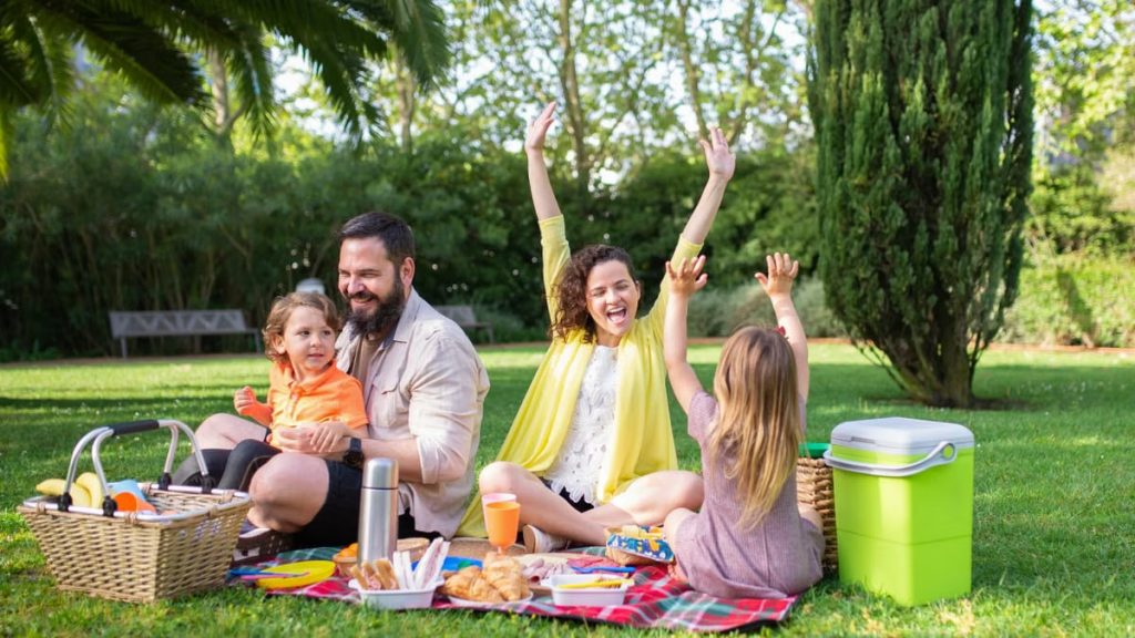 Happy family enjoying a sunny picnic with children on a blanket in a Portugal park.
